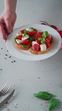 Domates, mozzarella ve açık arkaplanda fesleğen yaprakları. Crostino Caprese. Dikey video