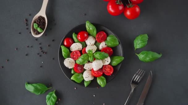 トップビュー黒を背景に新鮮なバジルの葉と熟したトマトとモッツァレラチーズとカプレーゼサラダ イタリア料理 — ストック動画