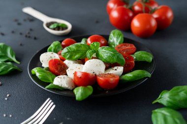 Dilimlenmiş domatesli İtalyan Caprese salatası, mozzarella peyniri, fesleğen, siyah arka planda zeytinyağı. Vejetaryen yemeği.