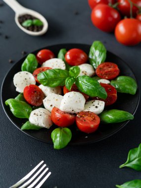 Olgun domatesli Caprese salatası ve siyah arka planda taze fesleğen yapraklı mozzarella peyniri. İtalyan yemeği.