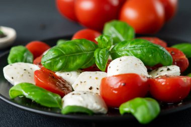 Olgun domatesli Caprese salatası ve siyah arka planda taze fesleğen yapraklı mozzarella peyniri. İtalyan yemeği. Yakın plan.