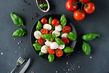 Olgun domatesli Caprese salatası ve siyah arka planda taze fesleğen yapraklı mozzarella peyniri. İtalyan yemeği. Üst görünüm