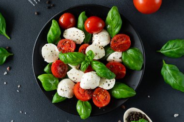 Olgun domatesli Caprese salatası ve siyah arka planda taze fesleğen yapraklı mozzarella peyniri. İtalyan yemeği.