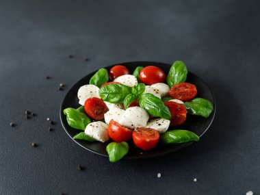 Olgun domatesli Caprese salatası ve siyah arka planda taze fesleğen yapraklı mozzarella peyniri. İtalyan yemeği.