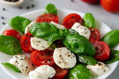 Olgun domatesli Caprese salatası ve açık arkaplanda taze fesleğen yapraklı mozzarella peyniri. İtalyan yemeği. Yakın plan.