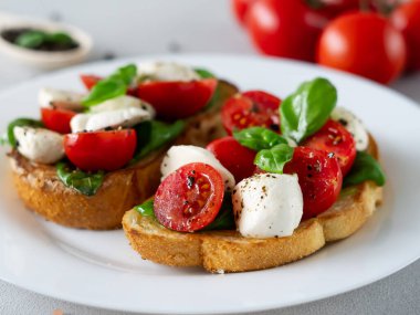 Açık arkaplanda taze domatesli, mozzarella ve fesleğen yapraklı Caprese Hughchetta 'nın yakın çekimi. Vejetaryen yemeği.