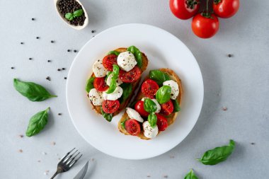 Taze domates, mozzarella ve açık arkaplanlı Basil yapraklı Caprese Hughchetta. Vejetaryen yemeği. Üst görünüm