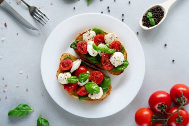 Taze domates, mozzarella ve açık arkaplanlı Basil yapraklı Caprese Hughchetta. Vejetaryen yemeği. Üst görünüm