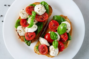 Taze domates, mozzarella ve açık arkaplanlı Basil yapraklı Caprese Hughchetta. Vejetaryen yemeği. Üst görünüm