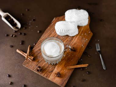 Cappuccino ve tahtada krema olan beyaz kekler. Kahverengi arka planda Latte Macchiato. Üst görünüm