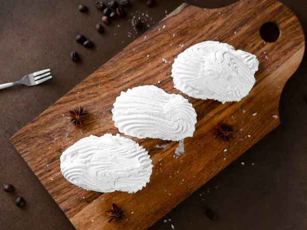 White Meringue cookies with cream on wooden board. Whipped egg cream cookies on brown background. Top view