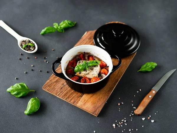 Feta peyniri, mavi soğan, kiraz domatesleri ve siyah arka planda baharatlarla zeytin yağında pişirilmiş fesleğen.