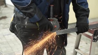 Metal tüpü Angle Grinder kullanarak kesen bir işçi. Parlak kıvılcımlar ve parıltılar