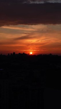 Büyük bir şehrin arka planında gün batımı. Şehir manzarasında turuncu ve kırmızı gökyüzü olan gün batımı binaların siluetleriyle