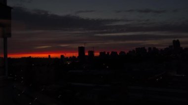 Şehir manzarasında turuncu ve kırmızı gökyüzü ve binaların siluetleriyle gün batımı. Büyük bir şehrin arka planında gün batımı