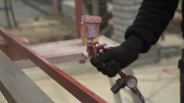 Zanaatkar sprey tabanca kullanarak metal bir yapı boyuyor. İşçi boya spreyi ve kompresörle boya uyguluyor. Ağır çekim.
