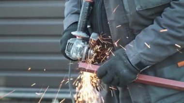 Metal tüpü Angle Grinder kullanarak kesen bir işçi. Parlak kıvılcımlar ve parıltılar