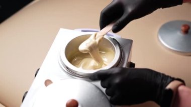 Usta, tüy dökme işleminden önce ısıtma balmumunu ahşap bir spatulayla karıştırıyor. Balmumuyla deplasyon
