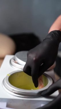 Saç kesmek için kullanılan sıcak altın cilası. Siyah koruyucu eldivenli tüy dökücü uzmanının ellerinde eritilmiş balmumuyla spatula bulunur. Eritme mumu aygıtı