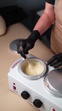 Usta, tüy dökme işleminden önce ısıtma balmumunu ahşap bir spatulayla karıştırıyor. Balmumuyla deplasyon