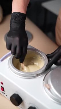 Usta, tüy dökme işleminden önce ısıtma balmumunu ahşap bir spatulayla karıştırıyor. Balmumuyla deplasyon