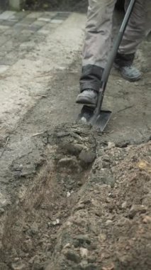 İşçi, bir kürekçi ile yere elektrik telleri döşeyip bir hendek kazıyor.