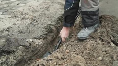 İşçi, bir kürekçi ile yere elektrik telleri döşeyip bir hendek kazıyor.