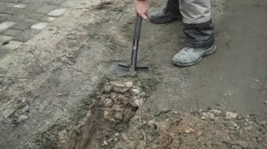 İşçi, bir kürekçi ile yere elektrik telleri döşeyip bir hendek kazıyor.