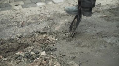 İşçi, bir kürekçi ile yere elektrik telleri döşeyip bir hendek kazıyor.