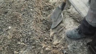 İşçi, bir kürekçi ile yere elektrik telleri döşeyip bir hendek kazıyor.