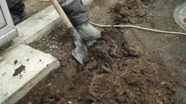 İşçi, bir kürekçi ile yere elektrik telleri döşeyip bir hendek kazıyor.