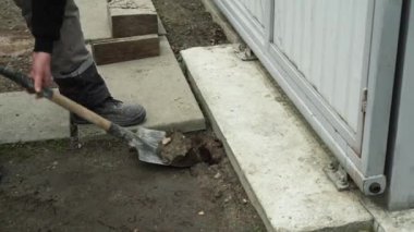 İşçi, bir kürekçi ile yere elektrik telleri döşeyip bir hendek kazıyor.