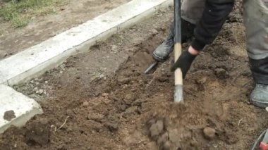İşçi, bir kürekçi ile yere elektrik telleri döşeyip bir hendek kazıyor.