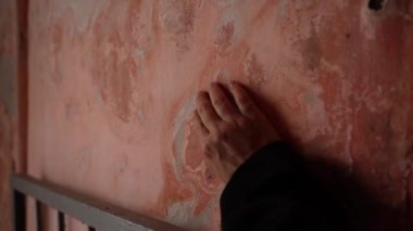 Terk edilmiş ya da yaşlanmış bir odada, yıpranmış pembe bir duvara nazikçe dokunan bir elin yakın çekimi.