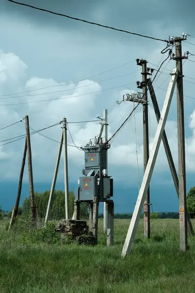 Beton direklerin üzerinde yeşil çimlerle çevrili ve çoklu elektrik hatları olan bir transformatör istasyonunun yer aldığı kırsal bir yer.