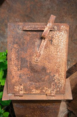 Eski, paslanmış metal bir kutunun ya da konteynırın tepeden tırnağa görüntüsü, zengin, benekli bir pas deseni içeriyor ve sağlam menteşelerle korunuyor ve çapraz metal şeritleri güçlendiriyor..