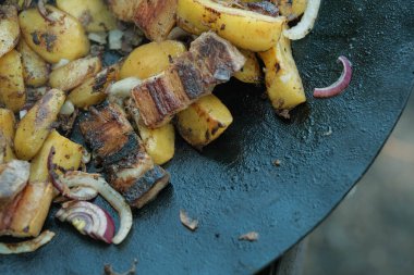 Küp patates, çıtır pastırma şeritleri ve kırmızı soğan dilimleri birbirine karışır. Bazıları kömürleşme ve yağ ile parlaklığı gösterir..