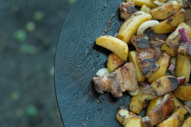 Küp patates, çıtır pastırma şeritleri ve kırmızı soğan dilimleri birbirine karışır. Bazıları kömürleşme ve yağ ile parlaklığı gösterir..