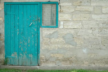 Canlı ama soyulan bir turkuaz ahşap kapı ve pencere çerçeve kontrastı desenli, yıpranmış taş ve beton duvarla.