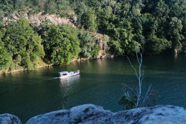 Dik, ormanlık bir kanyon duvarı ve çıplak bir dalla kayalık bir ön plan tarafından çerçevelenmiş koyu yeşil bir nehirde süzülür..