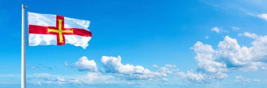 Guernsey Flag - state of Europe, flag waving on a blue sky in beautiful clouds - Horizontal banner