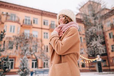 Orta yaşlı bir kadın, güzel bir ocak ayının karlı bir gününde kış şehrinin arka planında ve Noel ışıklarında karın tadını çıkarıyor.