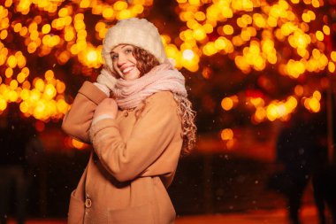 Akşamları kıvırcık saçlı, ışık ve süslenmiş bir Noel ağacıyla çevrili büyüleyici bir genç kadın. Noel arifesinde şenlikli şehirde gece yürüyüşü