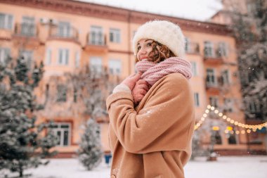 Orta yaşlı bir kadın, güzel bir ocak ayının karlı bir gününde kış şehrinin arka planında ve Noel ışıklarında karın tadını çıkarıyor.