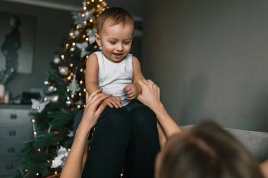 Anne küçük oğluyla şenlikli ev ortamında oynuyor. Mutlu çocuk Noel ağacının arka planına karşıdır. Kış tatili ve insanların konsepti