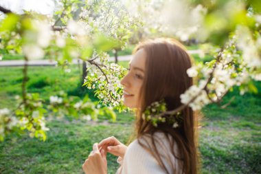 Genç ve güzel bir kadın gün batımında çiçek açan bir bahar bahçesinde dinleniyor. Sakinlik, kadınlık ve mutluluk kavramı.