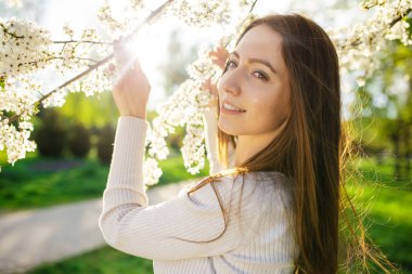 Gün batımında ilkbaharın erken saatlerinde çiçek açan bir elma ağacının yanında poz veren dişleri olan çekici bir kadının portresi.