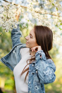 Baharda gün batımında çiçek açan elma ve kiraz ağaçlarıyla dolu güzel kokulu bir bahçede eğlenen genç bir kadın. Kadınlık, mutluluk ve aşk kavramı