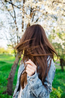 Gün batımında bahar aylarında çiçek açan elma ve kiraz ağaçlarıyla dolu güzel kokulu bir bahçede uçan saçlarıyla eğlenen genç bir kadının yakın çekimi. Uzun saçlarıyla oynayan bir kız.
