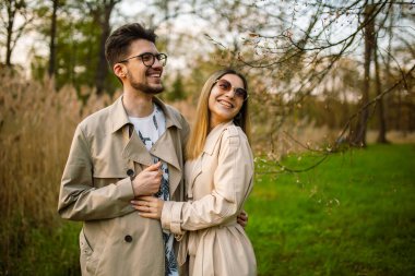 Bahar ormanı bahçesinde poz veren şık genç bir çift. Dişleriyle gülen kadın ve erkek. Rahatlama, gençlik, aşk, doğayla baş başa yaşam tarzı